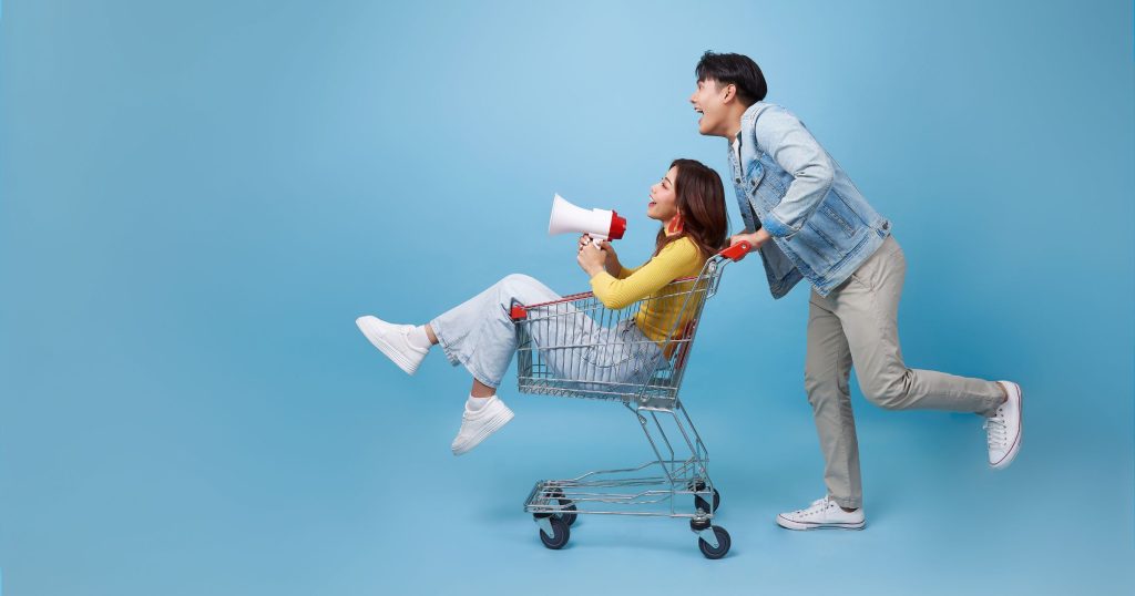 girl sitting inside shopping trolley holding megaphone asian man pushing shopping cart