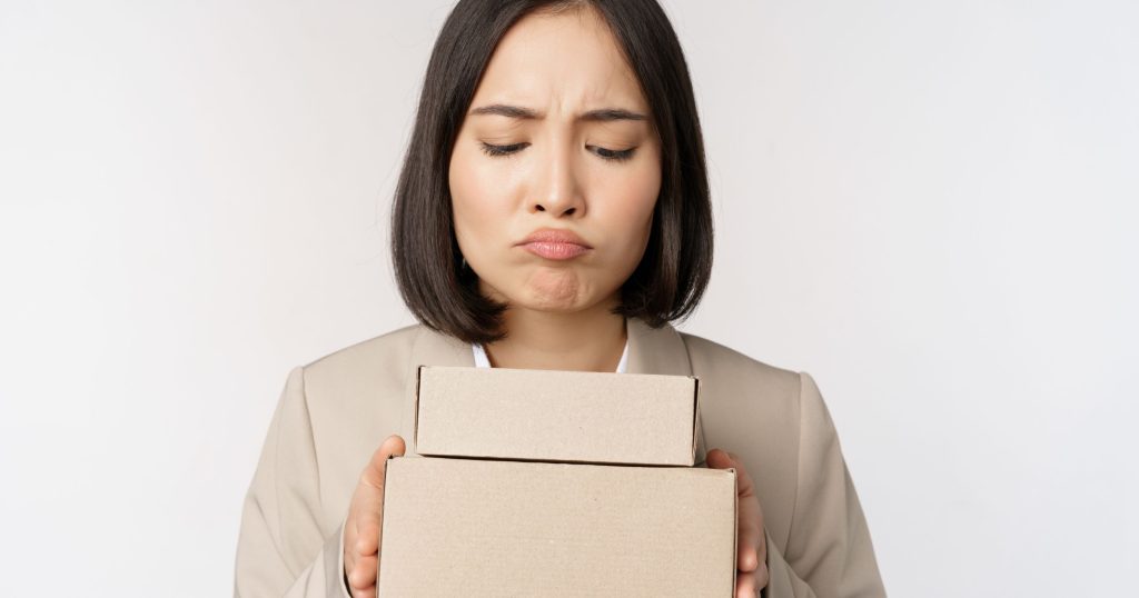 asian saleswoman female entrepreneur holding boxes looking sad